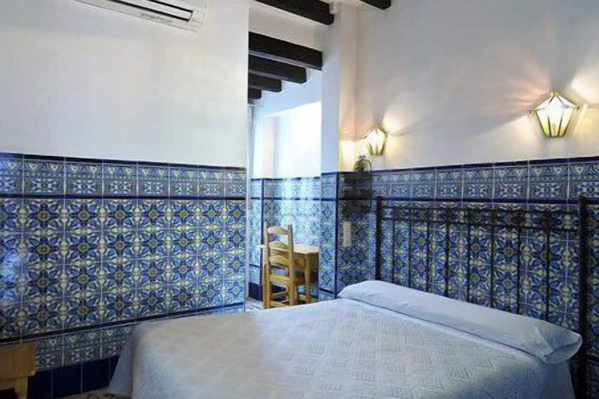 Una habitación con una cama, una silla y una pared con azulejos azules estampados.