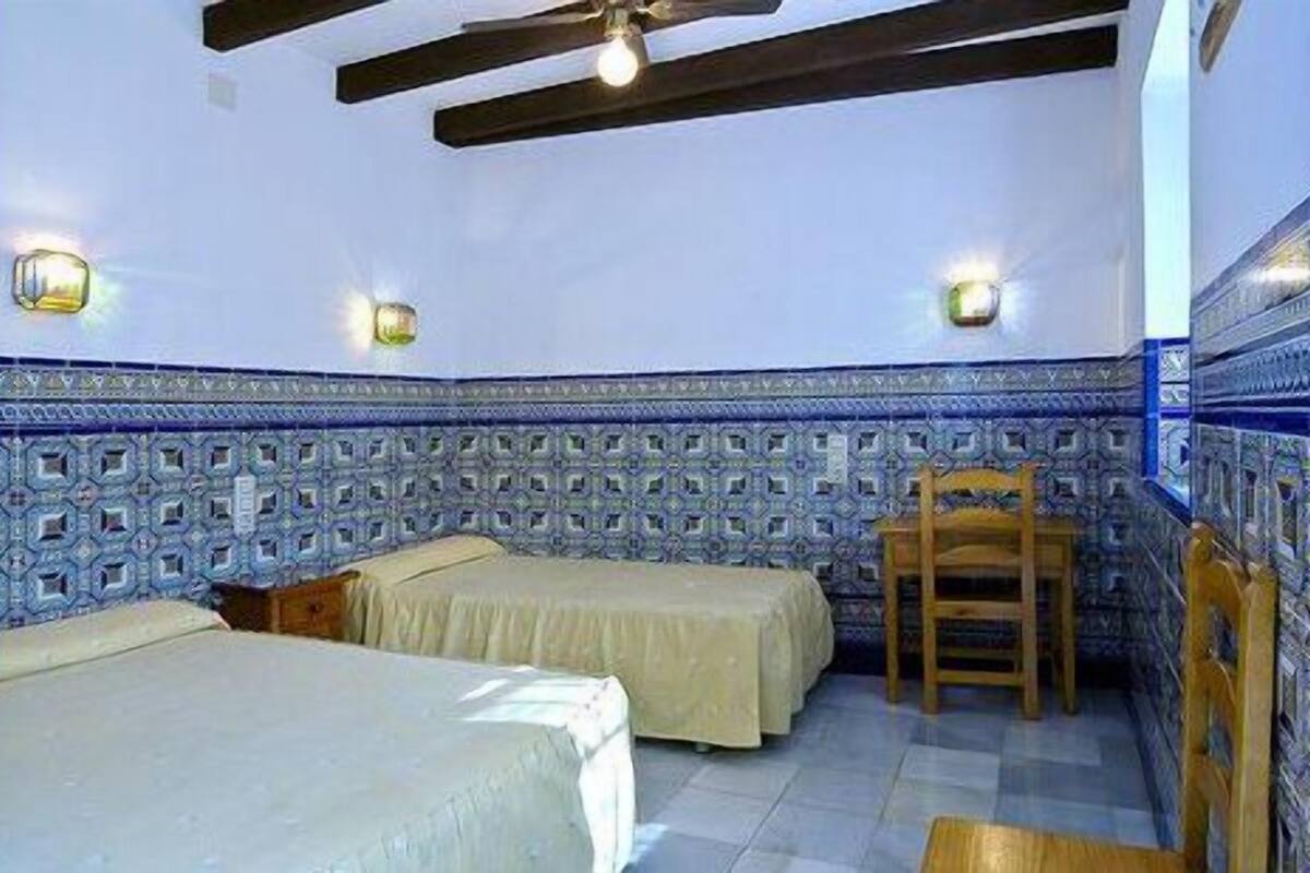 Una habitación con dos camas, una silla de madera y azulejos decorativos azules y blancos en las paredes.