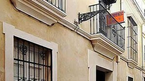 A building with barred windows, a black metal balcony railing, and a street lamp. - Hostal Lis I (Seville)