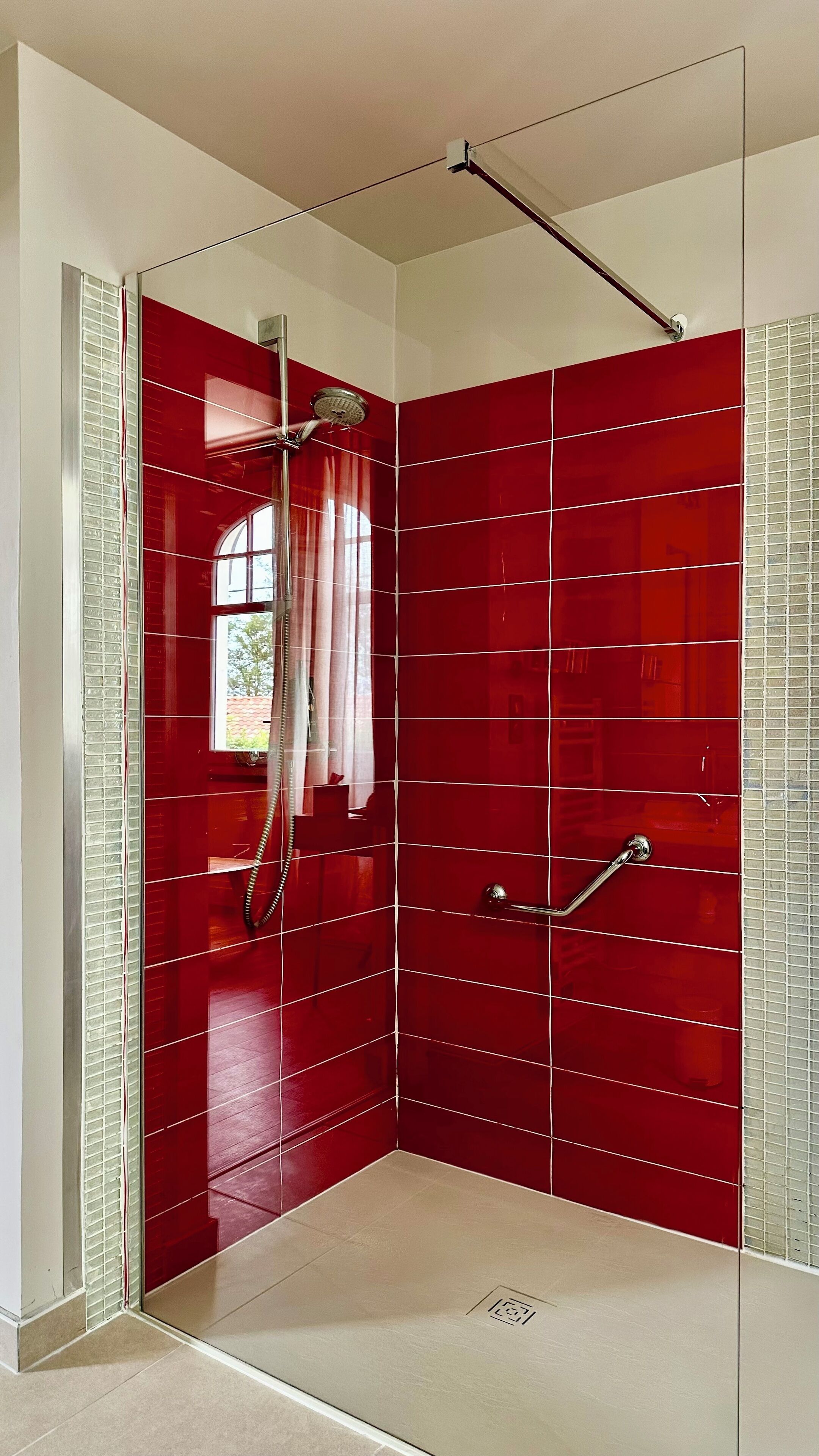 A walk-in shower with red tiles and a glass door.