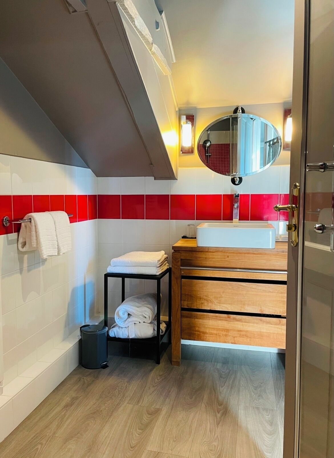 A modern bathroom with a wooden vanity, a white sink, and a red and white tiled backsplash.