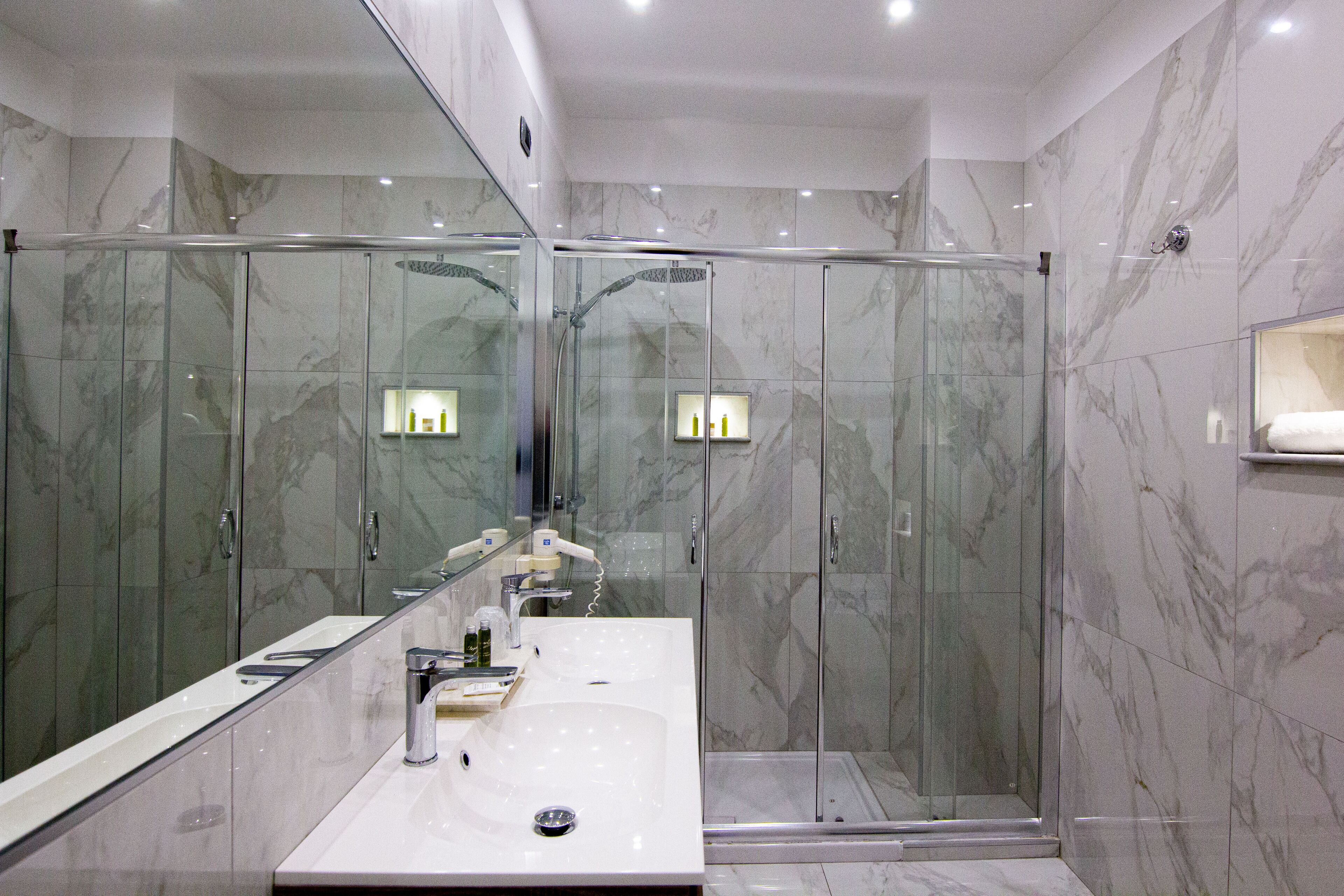 A modern bathroom with a glass-enclosed shower, a large mirror, and marble walls.
