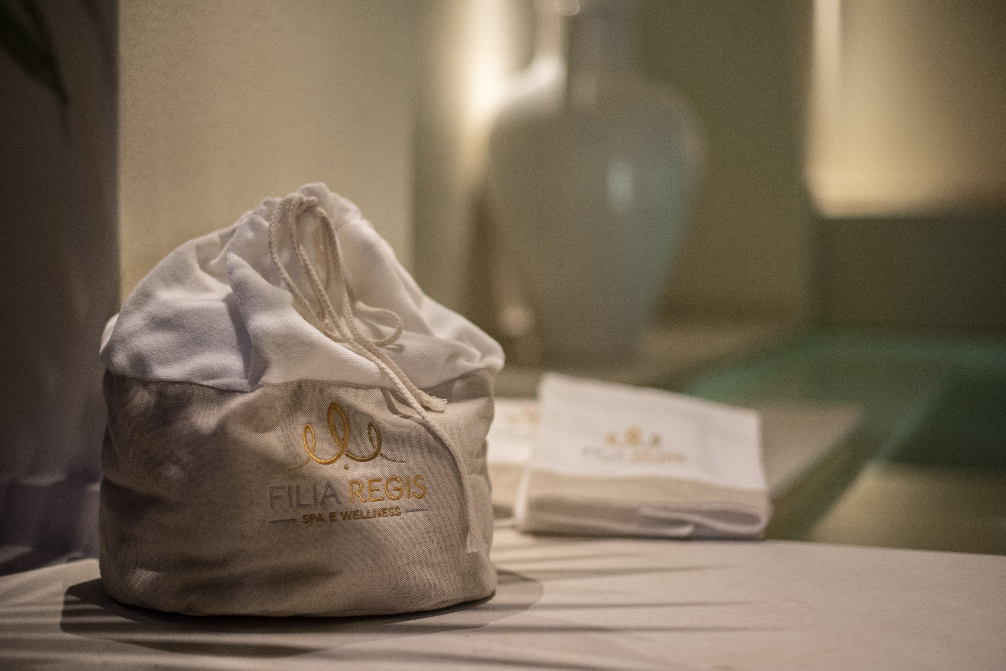 A white drawstring bag with "Fili Regis Spa & Wellness" text on a bed.