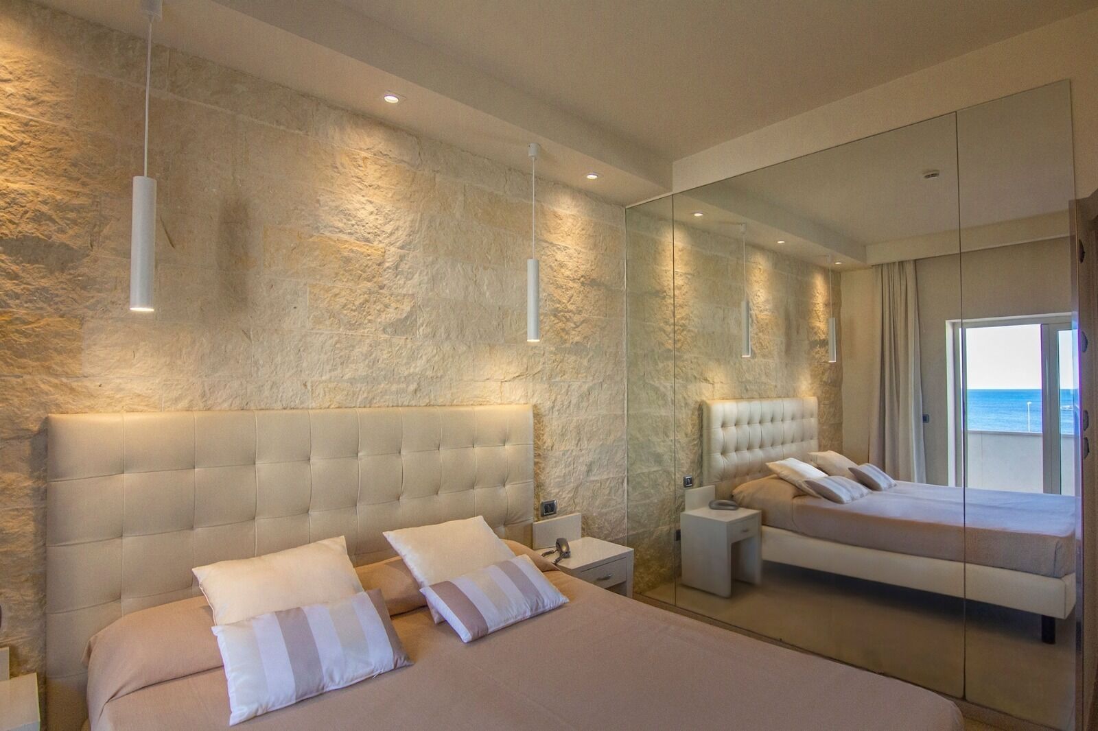 Une chambre moderne avec un grand lit, une table de chevet, une commode et un grand miroir qui reflète la pièce.