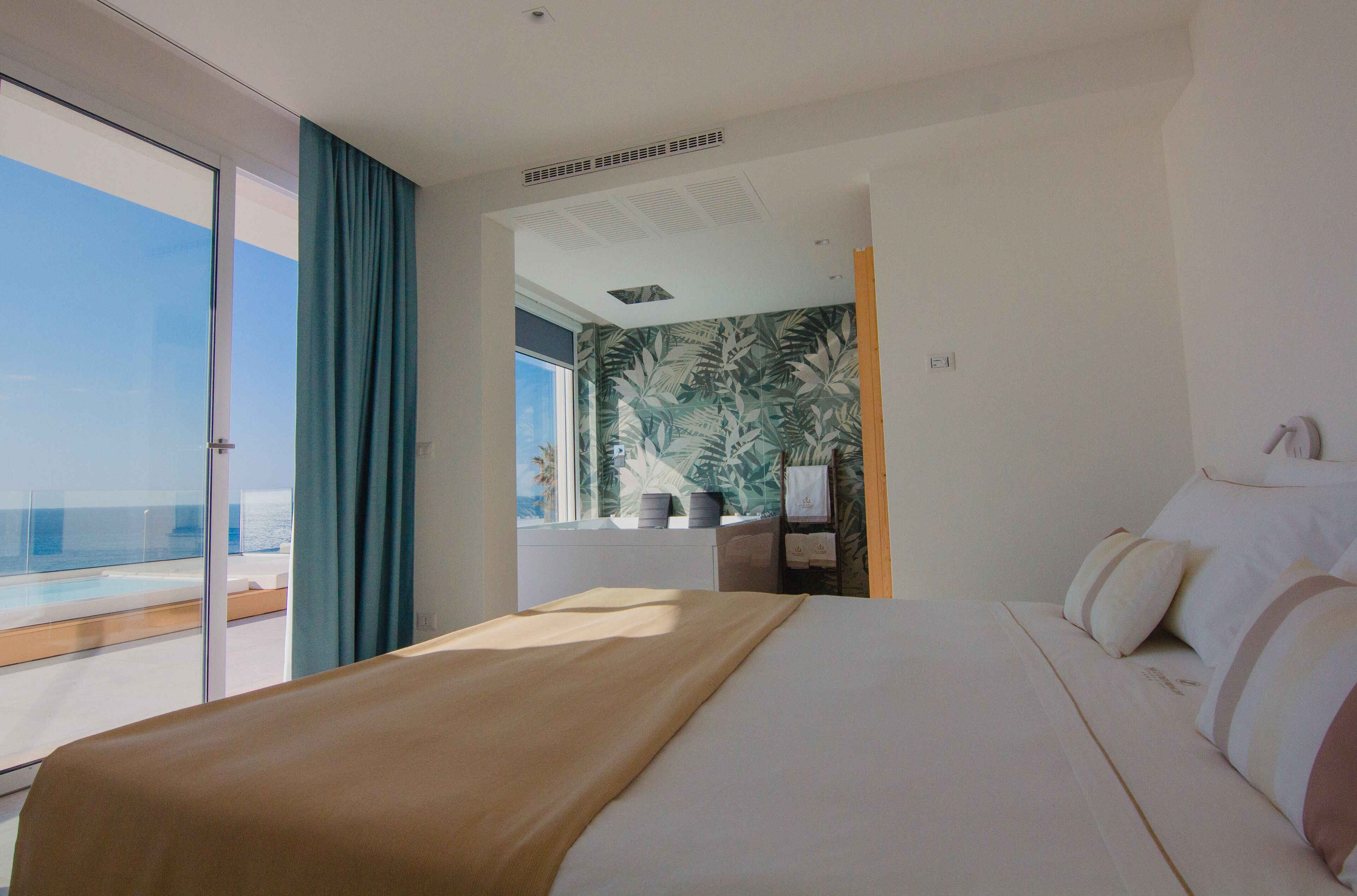 Una habitación de hotel con una cama grande, vista al océano y un papel tapiz tropical.