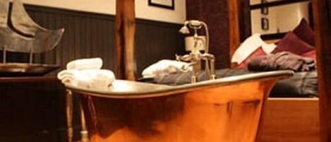 A bathroom with a vintage clawfoot bathtub, a wooden vanity, and a bed with a dark headboard.