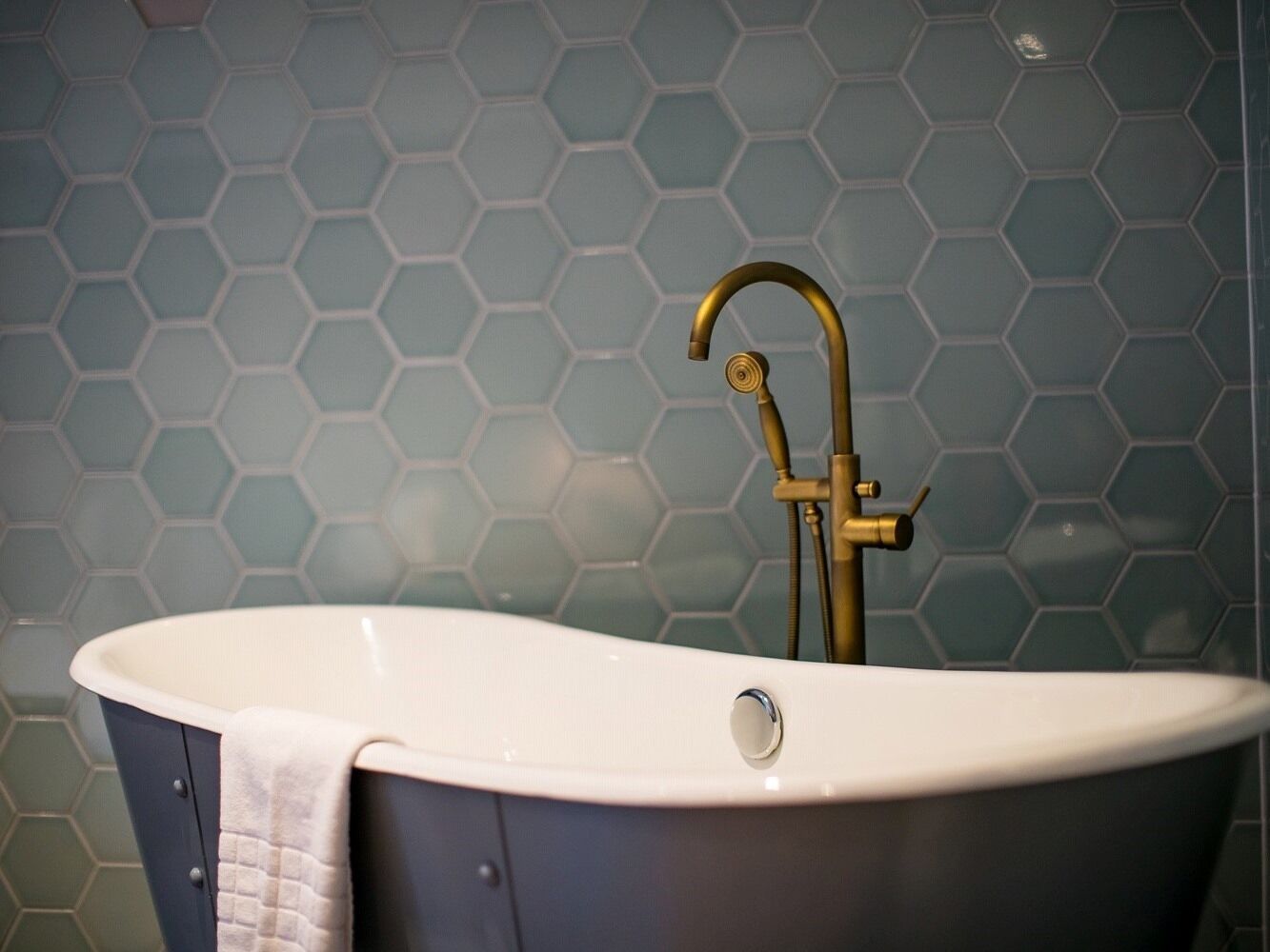 A bathtub with a gold faucet and a white basin, set against a hexagonal tile wall.