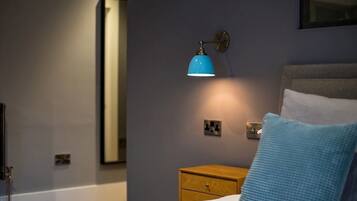 Et soveværelse med seng, et natbord, en blå lampe og et spejl.