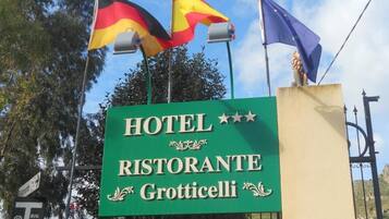 Señal para un hotel llamado "HOTEL RISTORANTE Grotticelli" con banderas de Alemania, Italia y la Unión Europea.