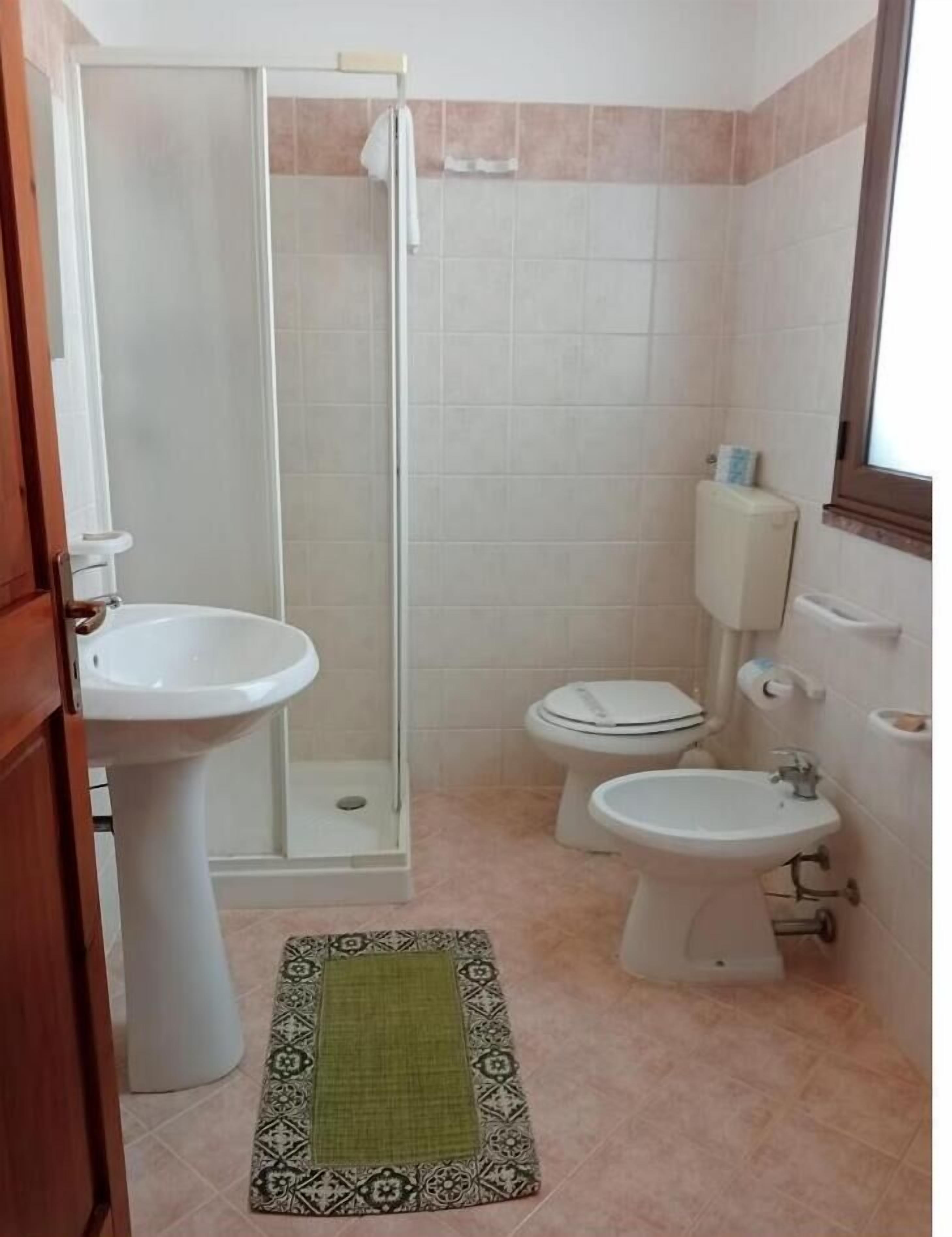 Une salle de bain avec une douche, deux toilettes, un lavabo et un porte-rouleau de papier toilette.