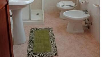 Une salle de bain avec une douche, deux toilettes, un lavabo et un porte-rouleau de papier toilette.