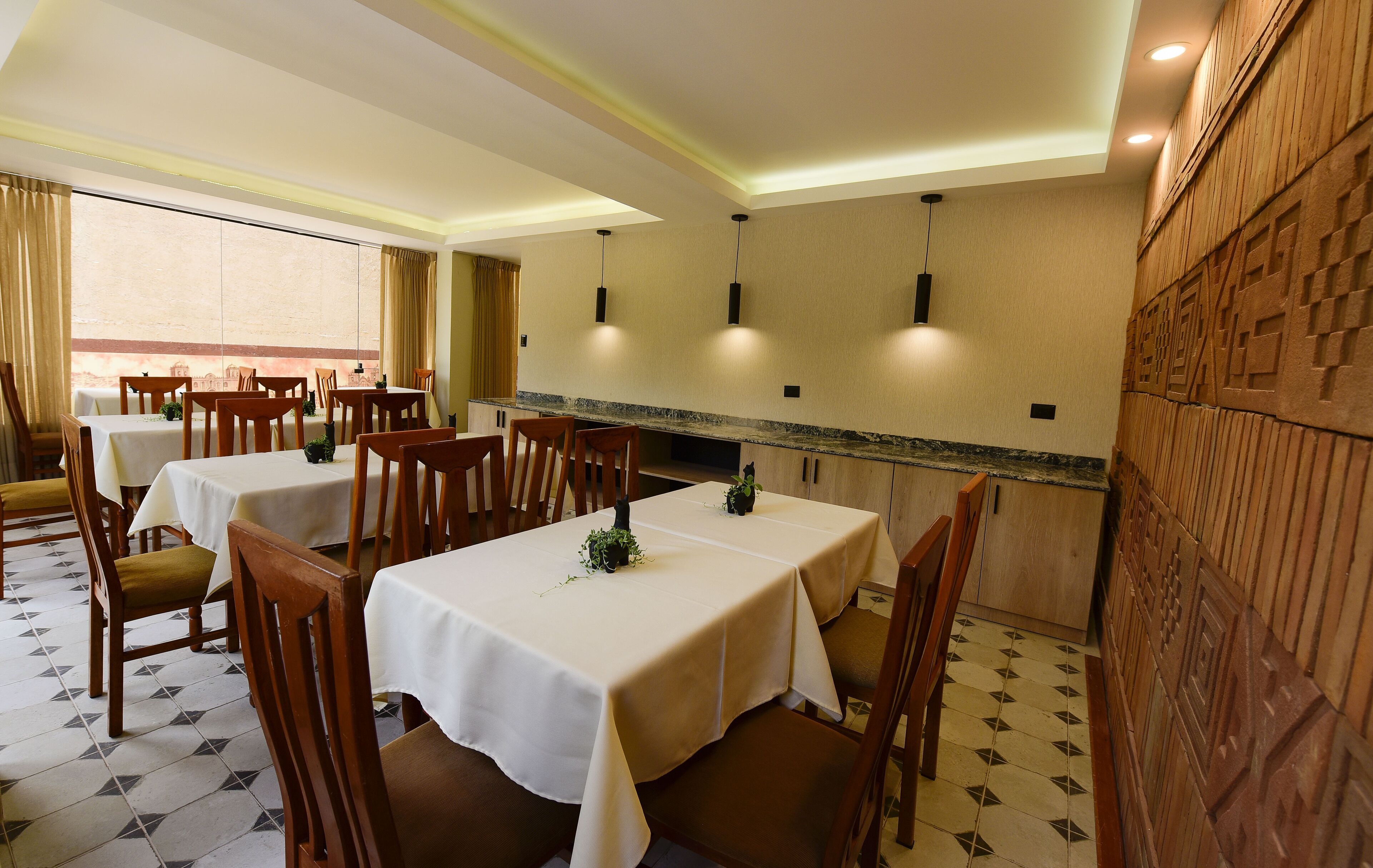 Un espace repas comprenant plusieurs tables et chaises, un coin cuisine doté d’un plan de travail en marbre et un panneau décoratif mural.