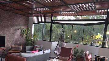 Un patio interno con parete in mattoni, un divano, due poltrone a dondolo, un tavolino e un'ampia finestra che offre vista sul verde circostante.
