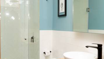 Een badkamer met een douchecabine van glas, een wit toilet, een wastafel met een zwarte kraan en een lijst met een afbeelding aan de muur.
