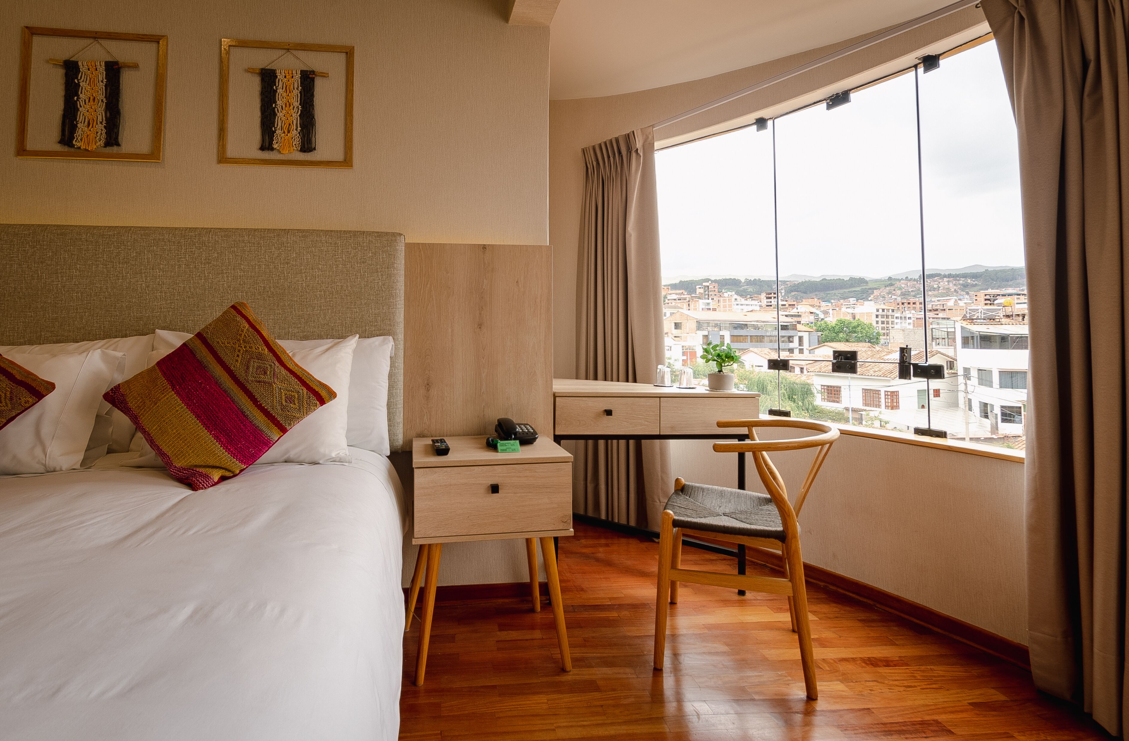 Habitación de hotel con cama, escritorio, silla y ventana grande con vista a la ciudad.