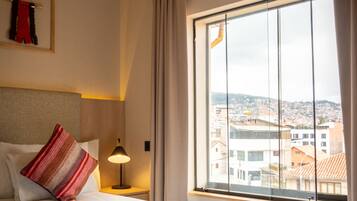Habitación de hotel con una cama grande, una mesita de noche, una lámpara y una ventana con vista a la ciudad.