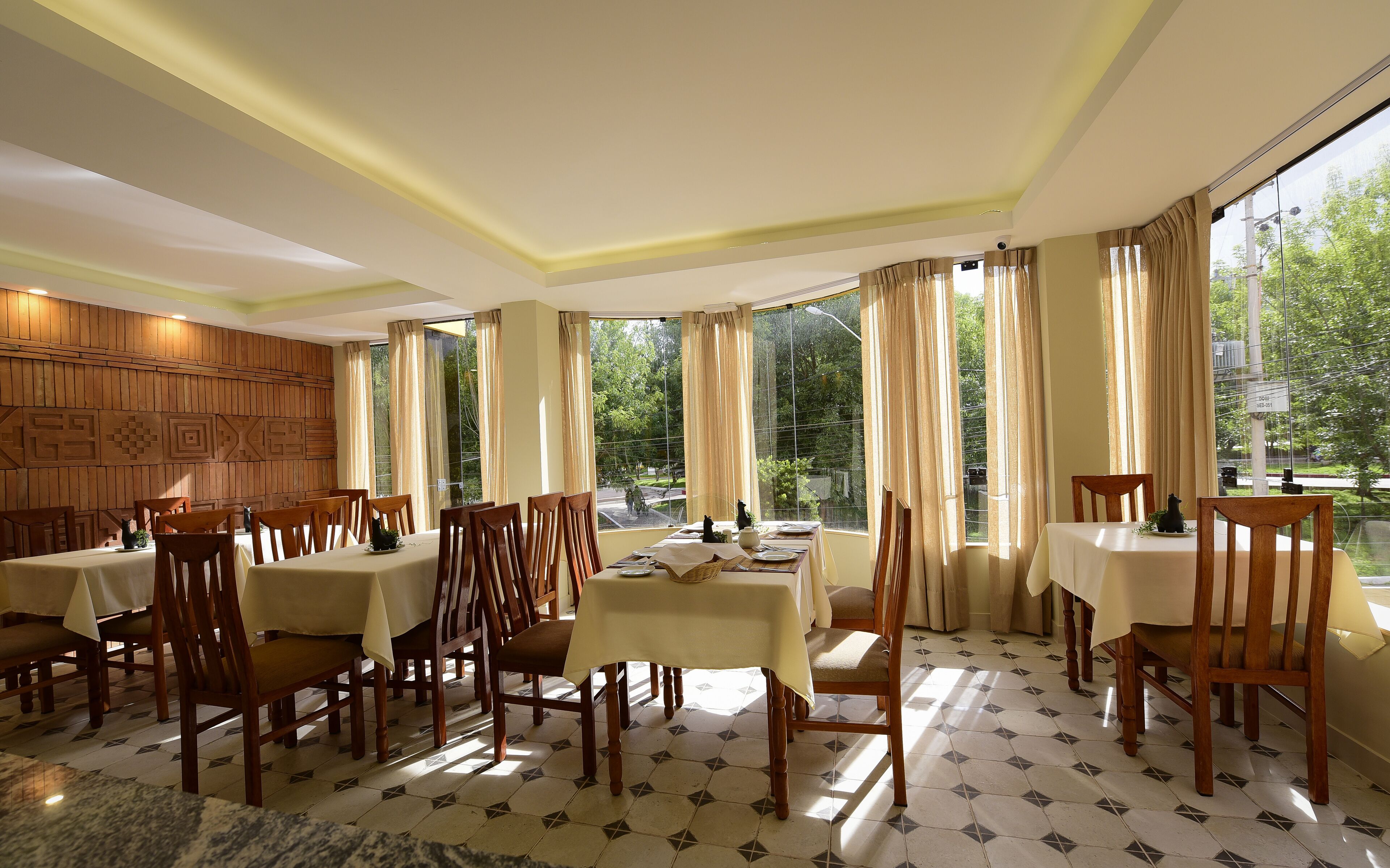 A dining area with multiple tables and chairs, large windows with curtains, and a patterned wall.