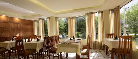 A dining area with multiple tables and chairs, large windows with curtains, and a patterned wall.