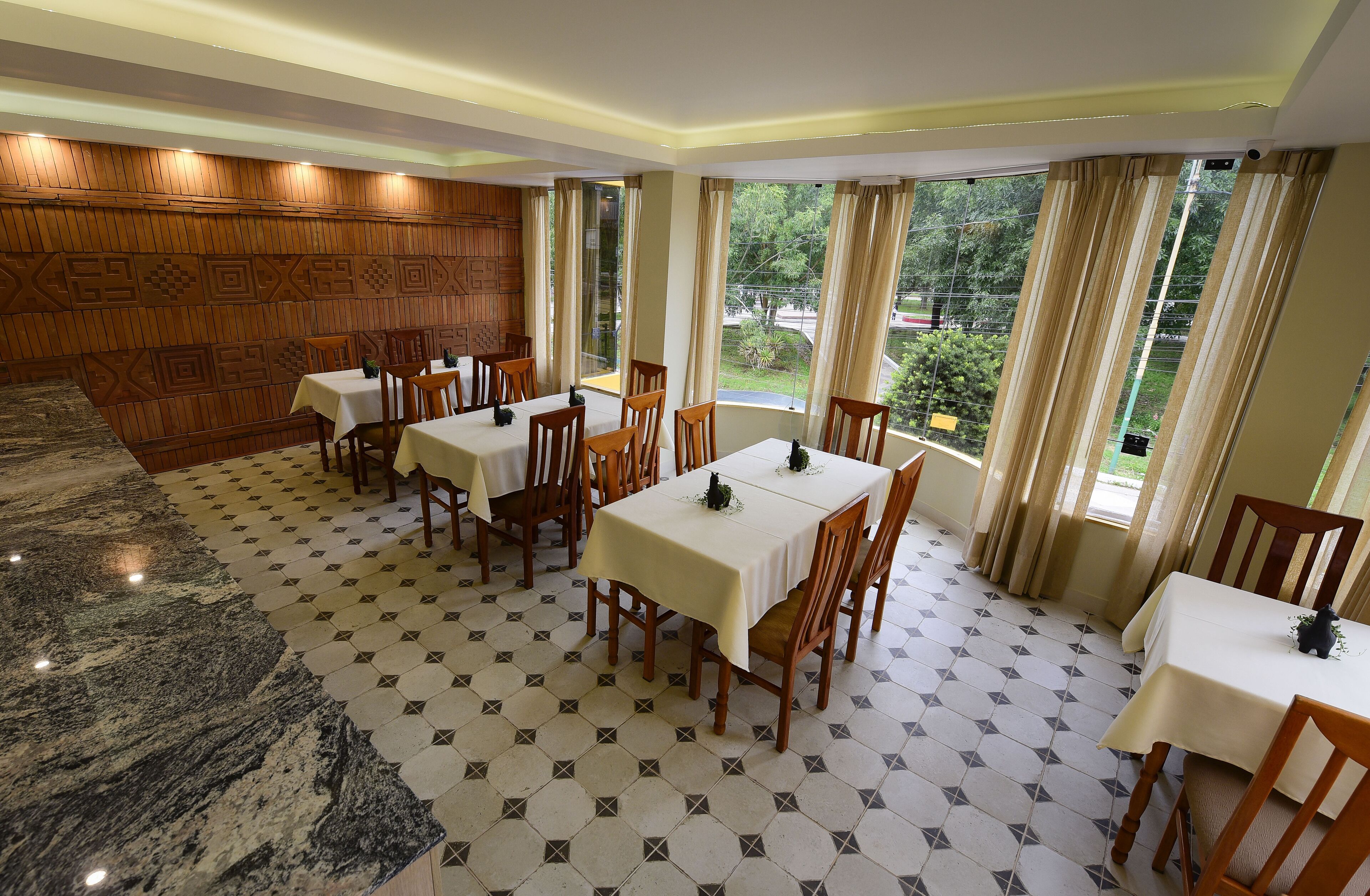 A dining area with tables and chairs, a patterned floor, and a view of greenery outside.