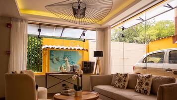 Ein modernes Wohnzimmer mit Sofa, Sessel und Couchtisch, mit einem großen Fenster und Blick auf Grünflächen sowie einem geparkten Van vor dem Haus.