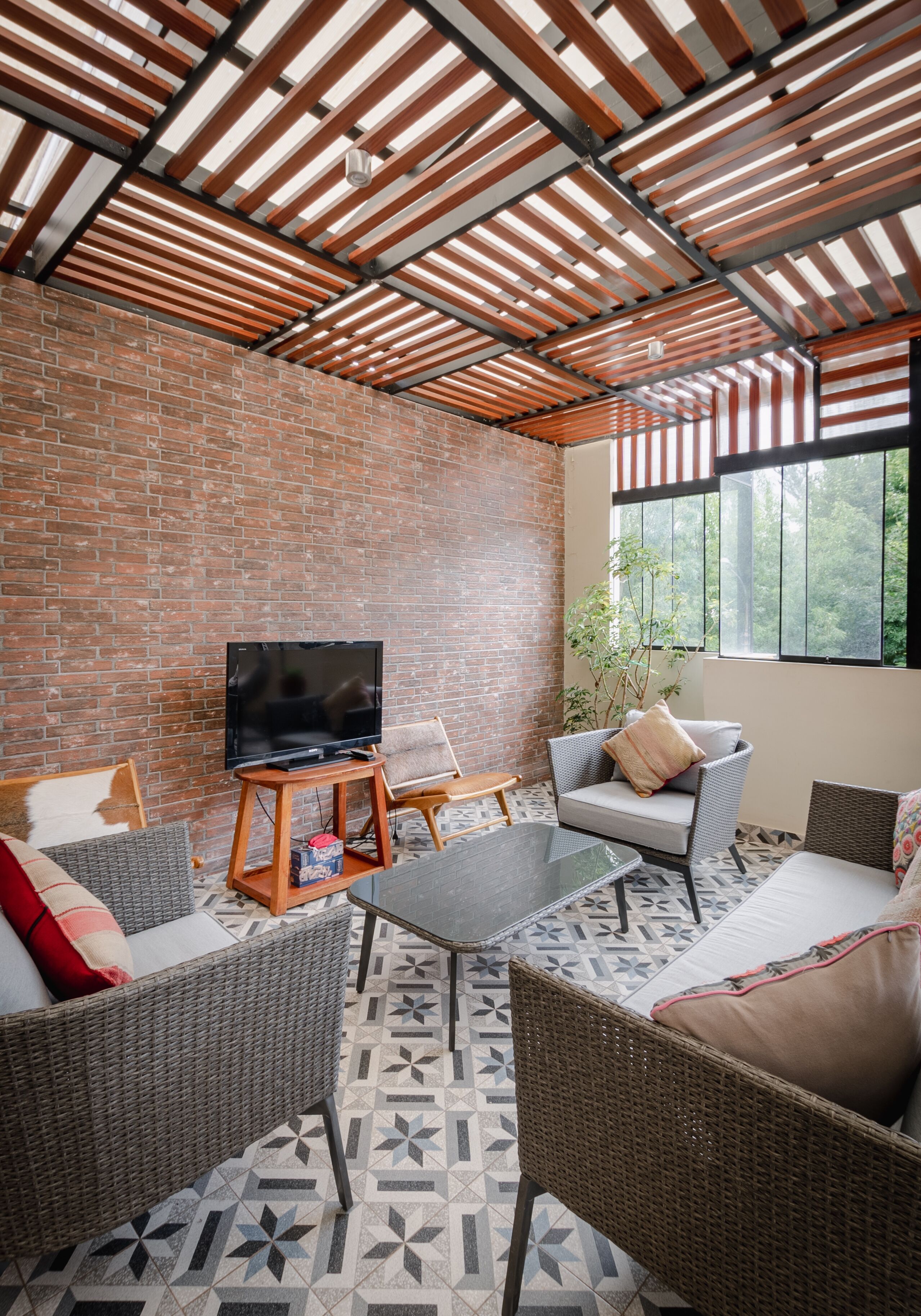 A cozy outdoor seating area with wicker furniture, a flat-screen TV, and a brick wall.