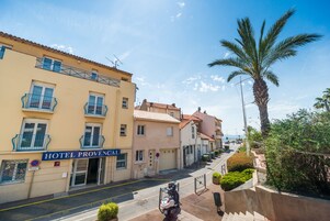Vista de la calle del Hotel Provençal, con cielo despejado, una palmera y una moto estacionada.