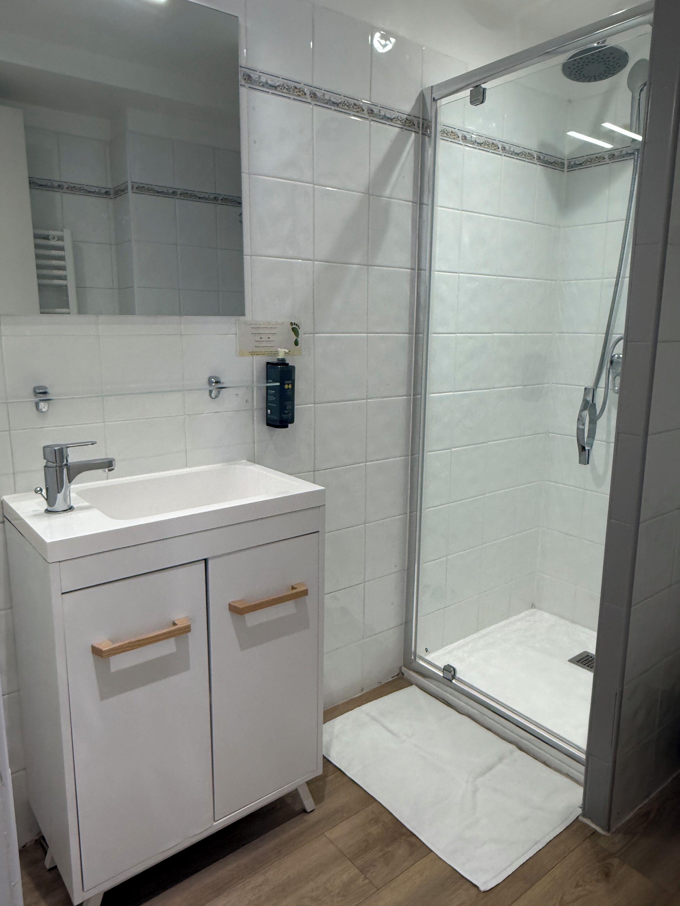 A bathroom with a white sink, mirror, and shower enclosure.