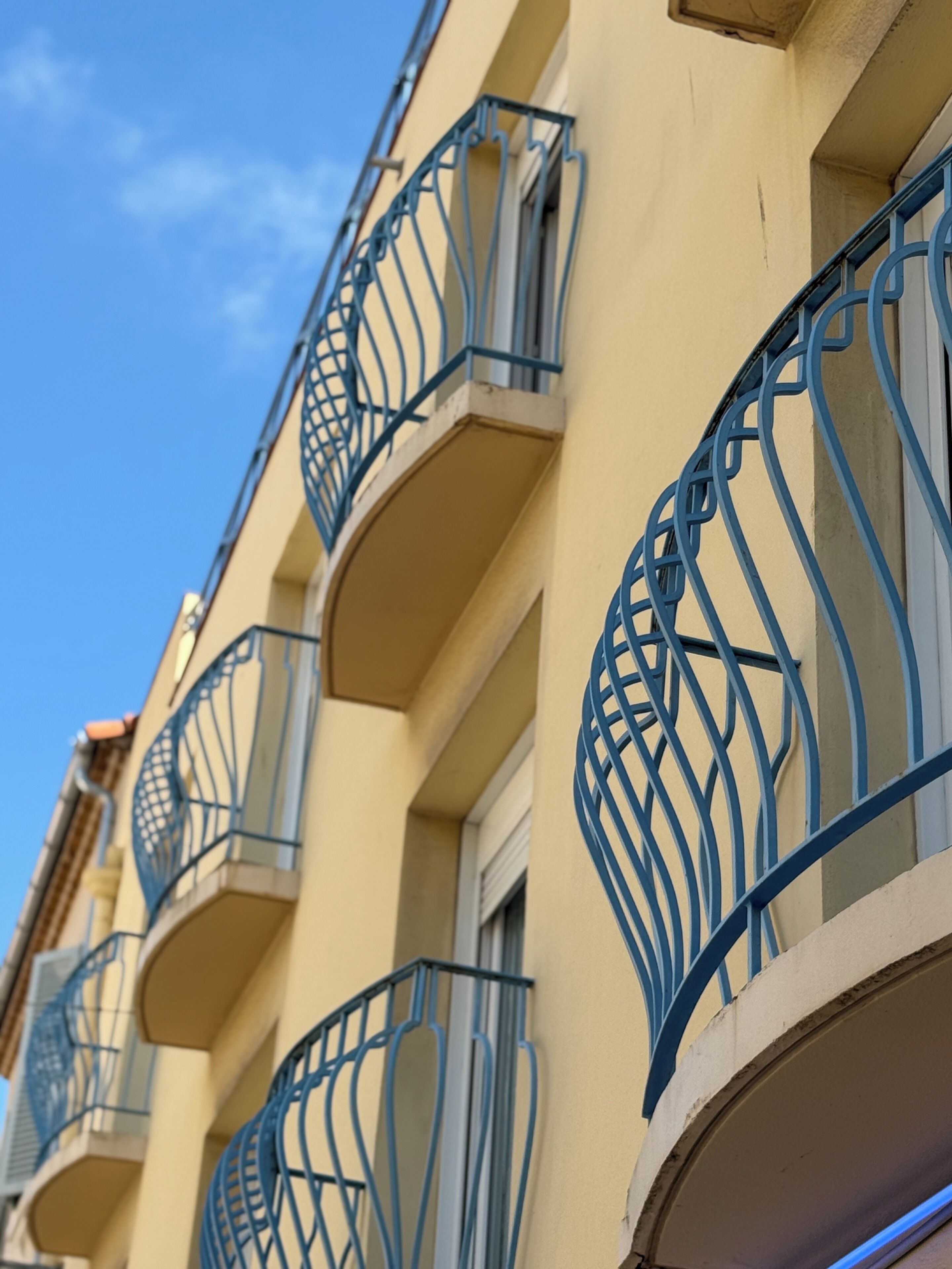 A row of balconies with metal railings, a beige building facade, and a clear blue sky.