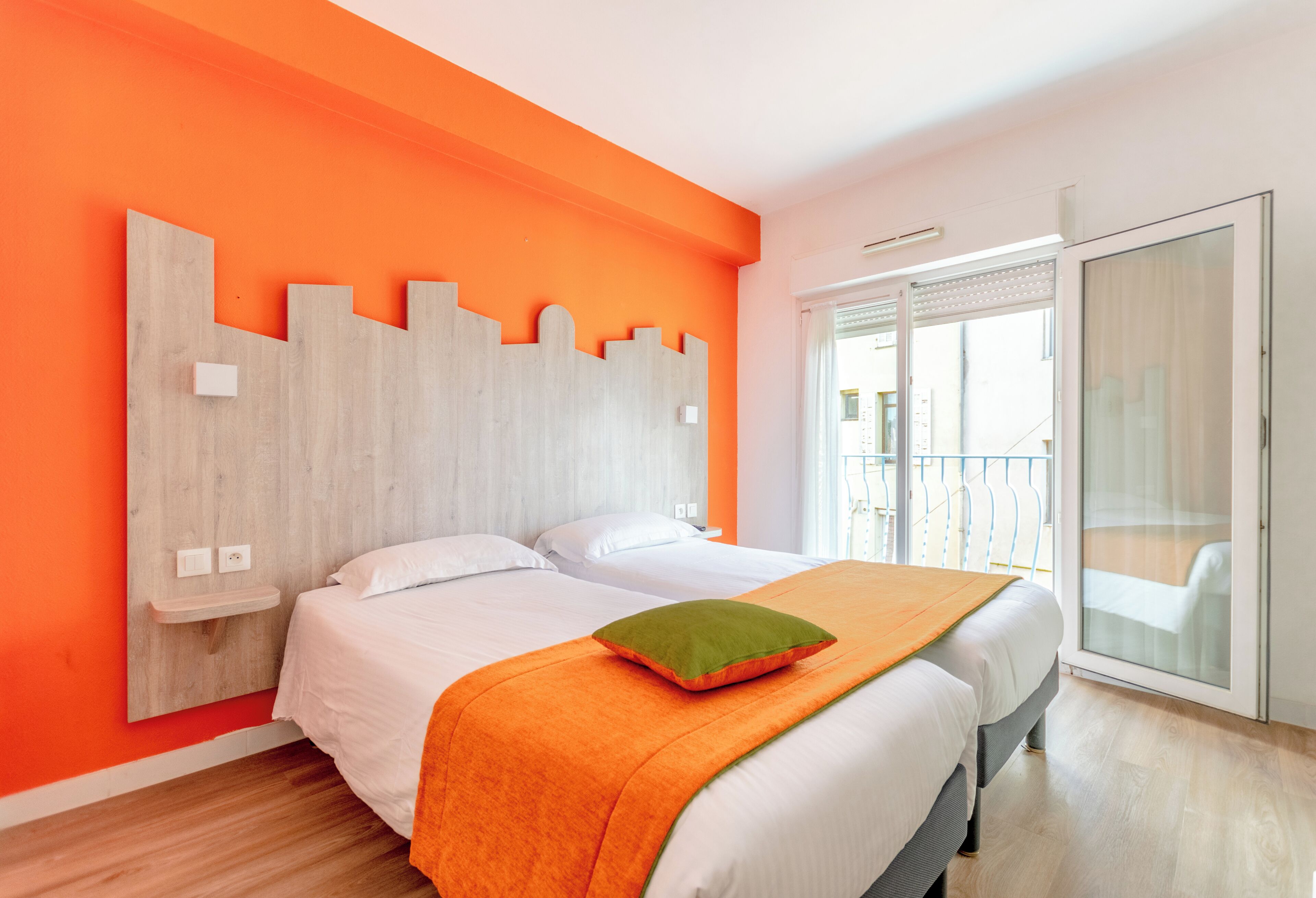 A hotel room with a bed, a wooden headboard, a balcony, and a large window.