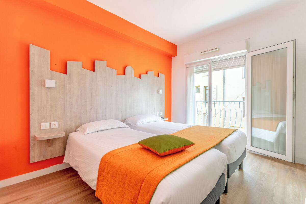 A hotel room with a bed, a wooden headboard, a balcony, and a large window.