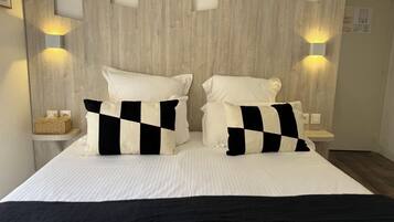 Una cama con dos almohadas, una mesita de noche y luces fijadas en la pared.