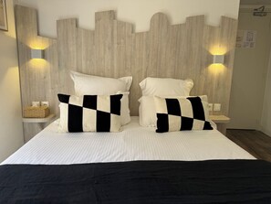 A bed with two pillows, a bedside table, and wall-mounted lights. - Provençal Hotel (Saint-Raphael)