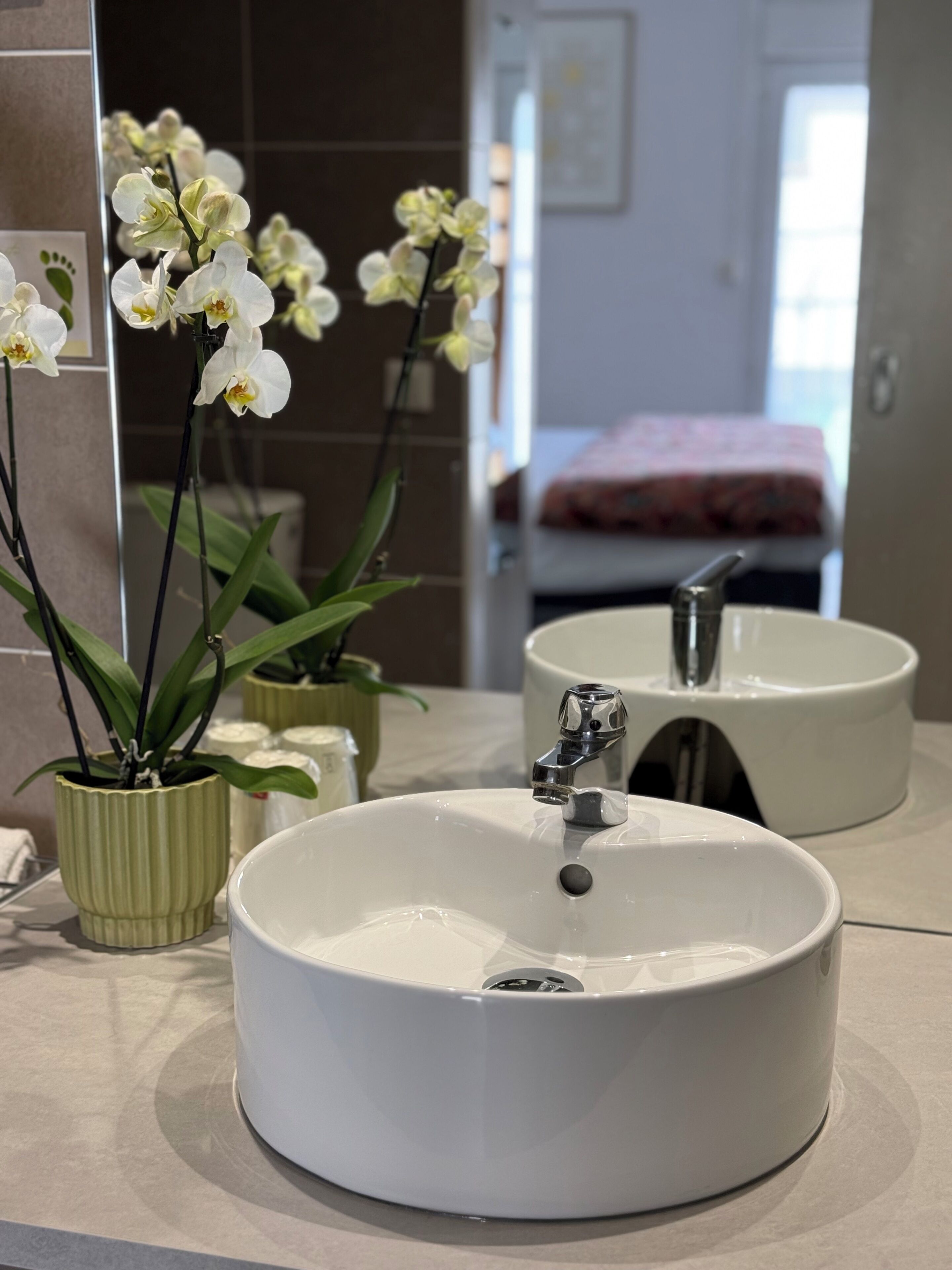 A bathroom with a white sink, a mirror, and orchids.