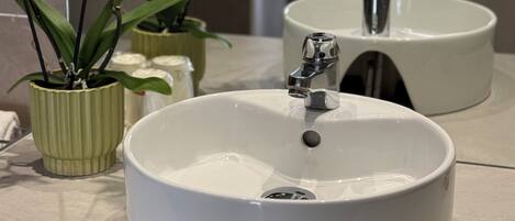 A bathroom with a white sink, a mirror, and orchids.
