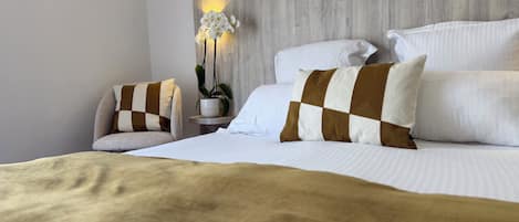 Habitación de hotel ordenada con cama, almohadas, una mesita de noche con una planta y un aplique de pared.