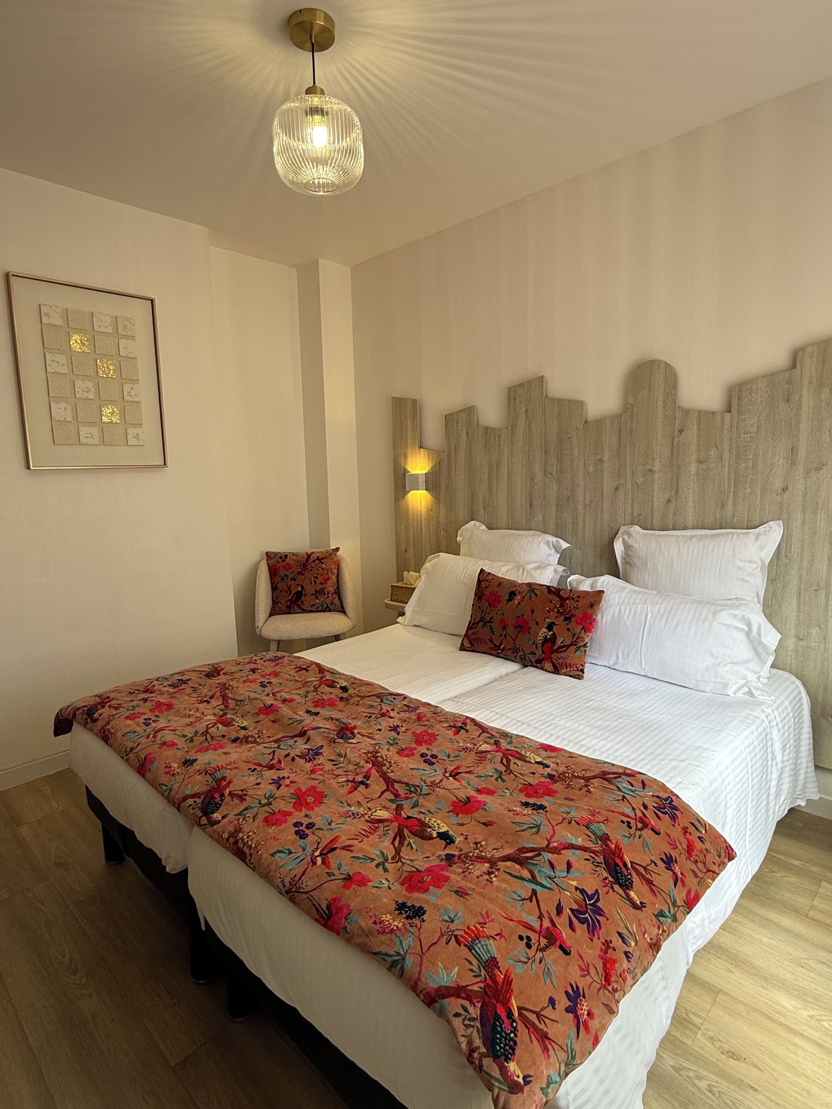 Une chambre à coucher avec un grand lit, une chaise, une lampe fixée au mur et un luminaire au plafond.