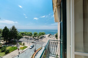 Un balcón con vistas a una calle costera, árboles y un cielo despejado.