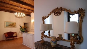 A room with a wooden ceiling, a chandelier, a sofa, a white cabinet, a mirror with an ornate frame, and a vase on a dark wooden table. - Bed & Breakfast Relais San Giacomo (Maiori)