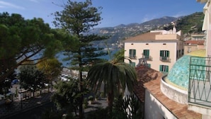 A coastal building with a curved roof, a balcony with a green railing, and a view of the sea and distant hills. - Bed & Breakfast Relais San Giacomo (Maiori)