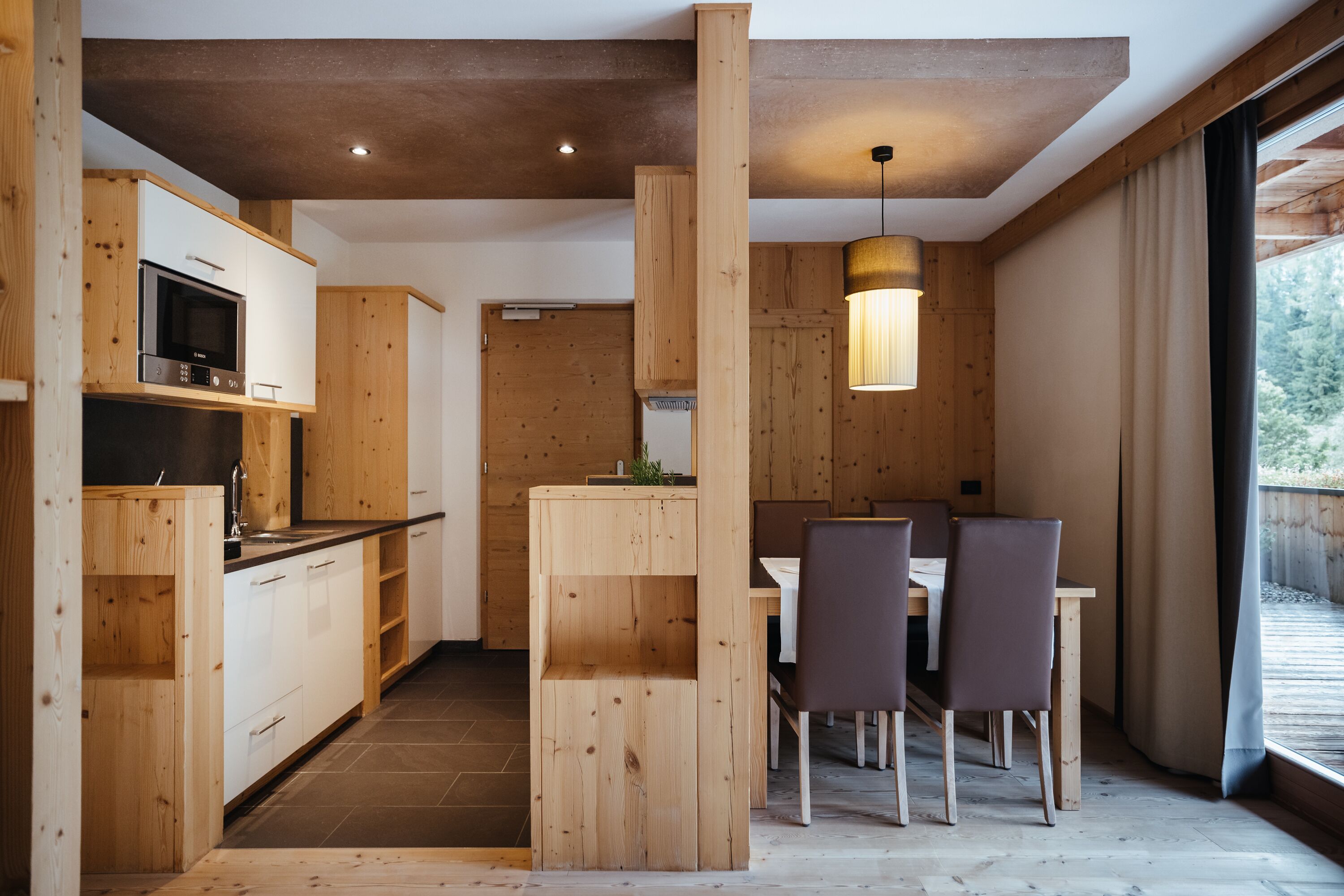 A modern kitchen with wooden cabinets, a built-in microwave, and a dining area with a table and chairs.