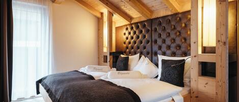 A wooden-framed bedroom with a tufted headboard, a large bed with white linens, and a window with sheer curtains.