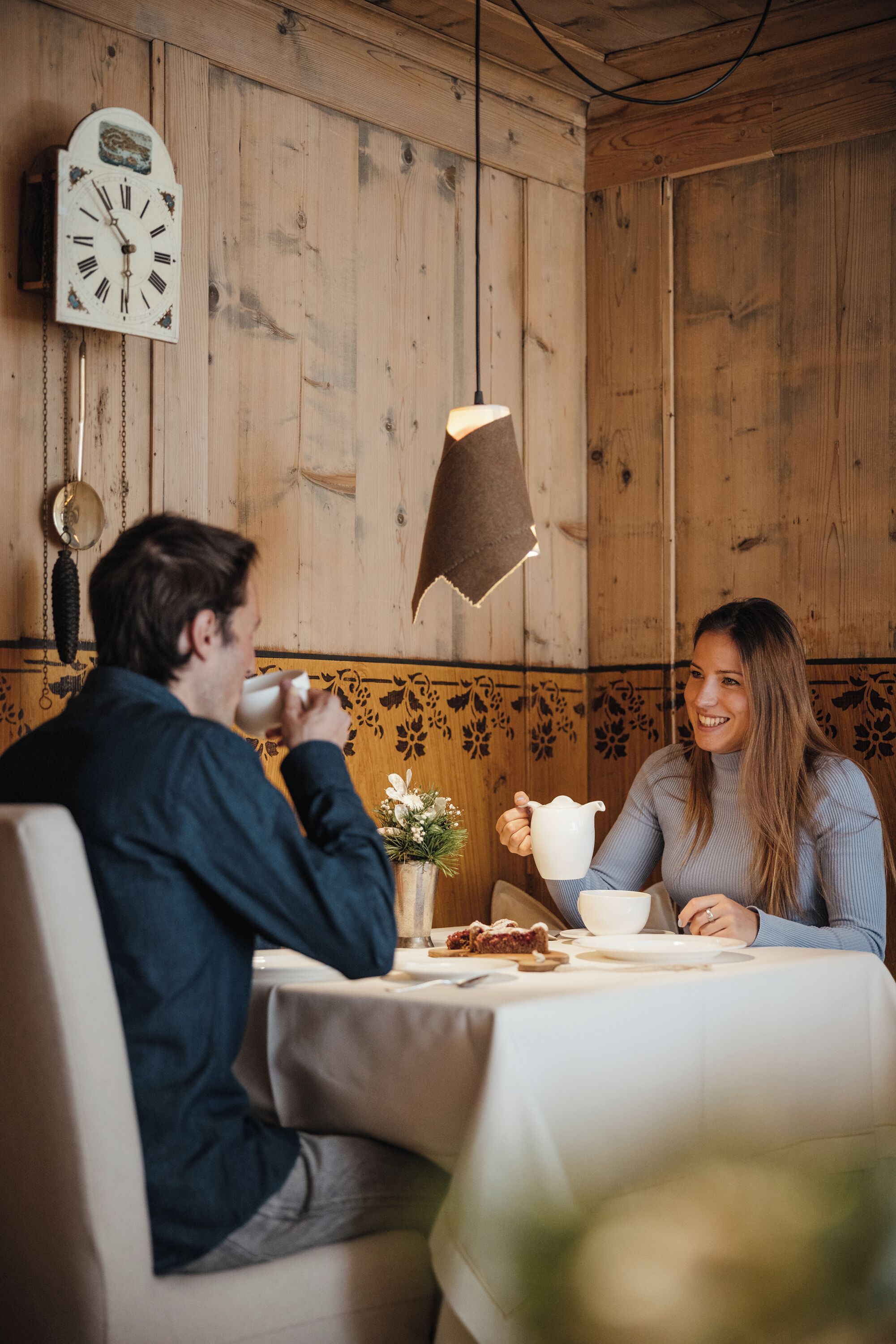 Ein Holzinterieur mit einer Uhr, einem Tisch mit weißer Tischdecke und einer Blumenvase.