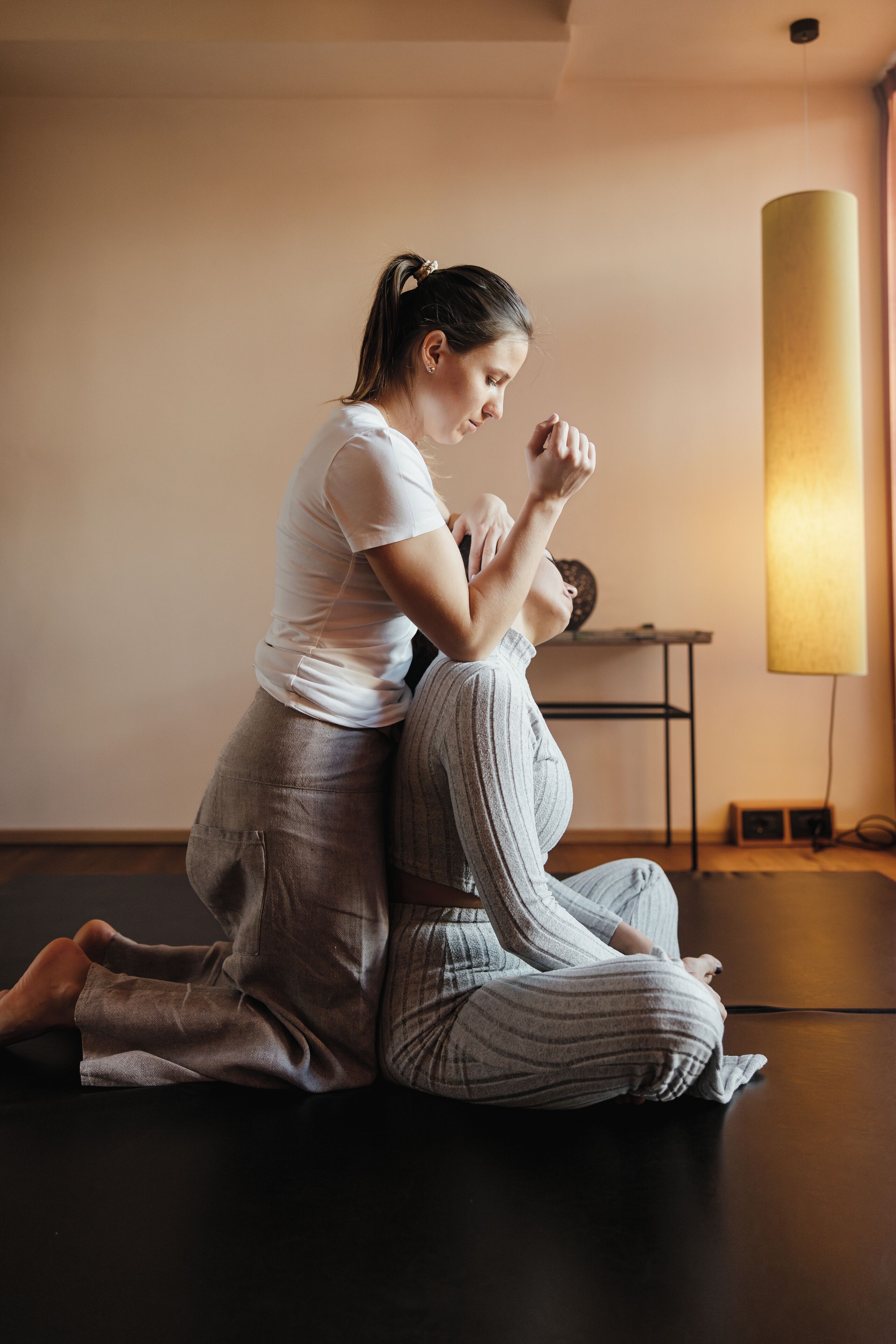 A person performing a yoga pose on a mat in a room with a lamp and a shelf.