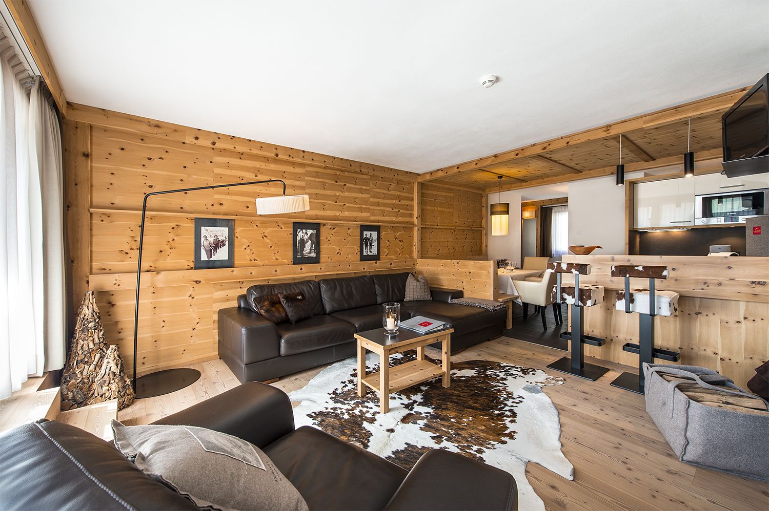 Interior moderno de una cabaña de troncos con sala de estar, sofá, mesa de centro y comedor con cocina al fondo.