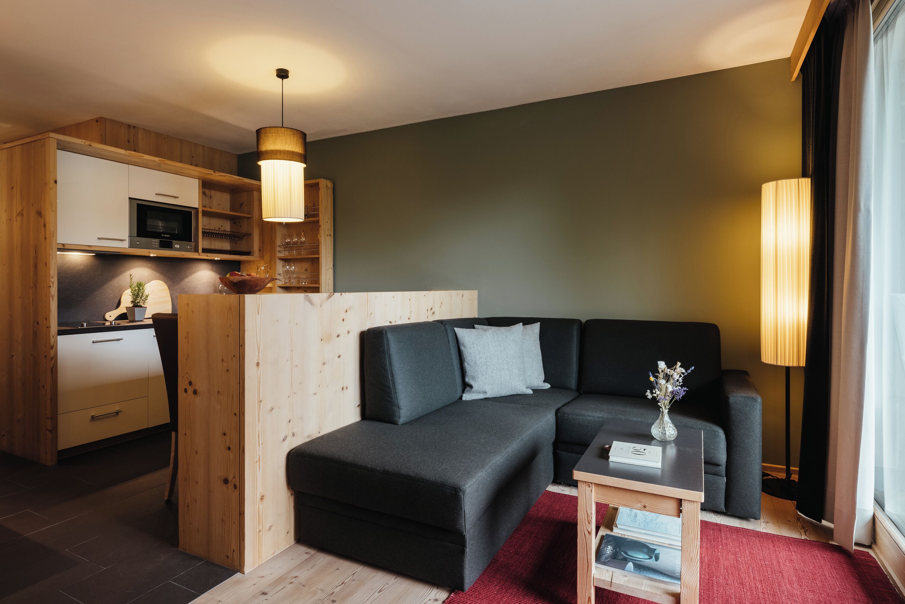 En moderne stue med en hjørnesofa, et lille bord og et køkkenområde med træskabe og en mikrobølgeovn.