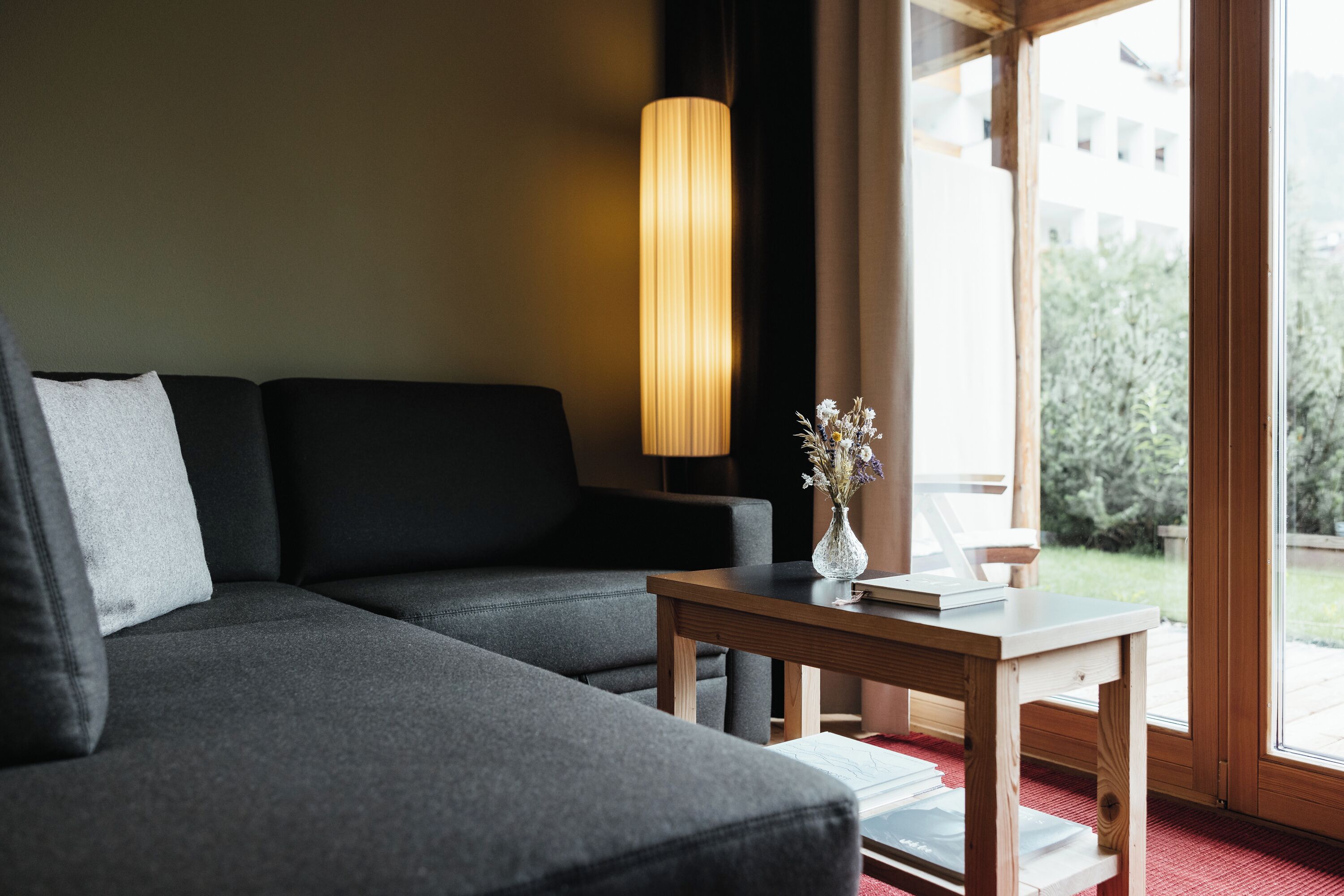 A modern living room with a dark grey sofa, a wooden side table with a vase of flowers, and a tall floor lamp.