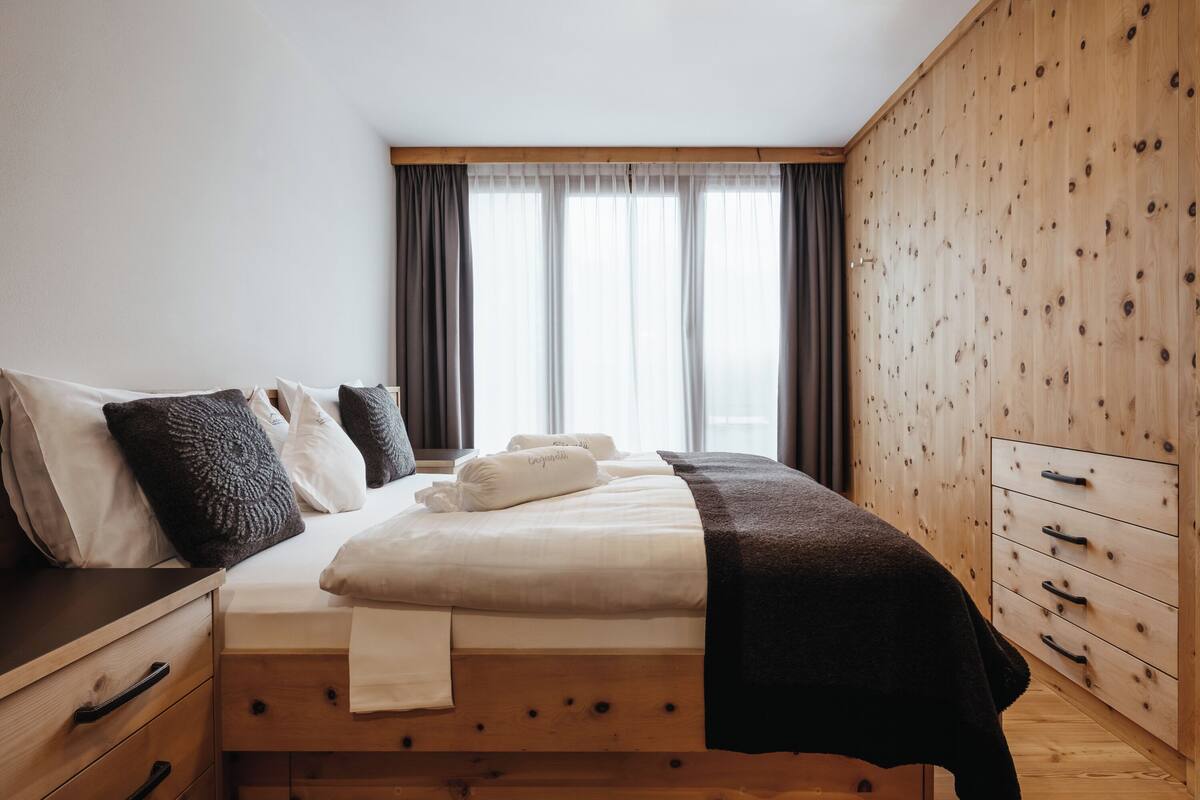 A bedroom with a wooden bed, a wooden wardrobe, and a window with curtains.