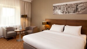Une chambre d’hôtel avec un grand lit, deux fauteuils, une petite table ronde et une lampe.