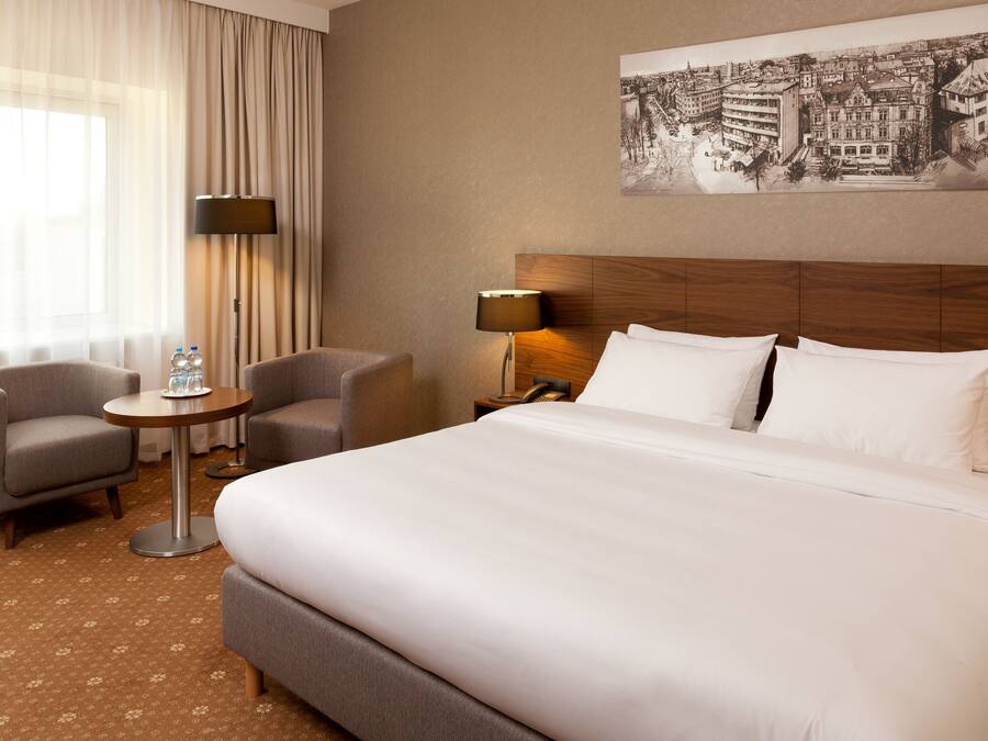 A hotel room with a large bed, two armchairs, a small round table, and a lamp.