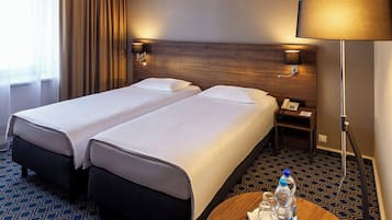Habitación de hotel con dos camas, una mesita de noche con lámpara, teléfono y un recipiente con botellas de agua.